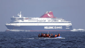 Un bote repleto de migrantes se cruza con un ferri de pasajeros en Sikaminias, Grecia, en aguas del mar Mediterráneo. Carl Corte / Getty Images